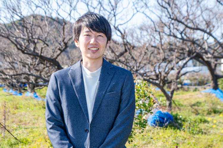 梅の圃場の前で笑顔で写真に写る株式会社うめひかり代表の山本 将志郎さん
