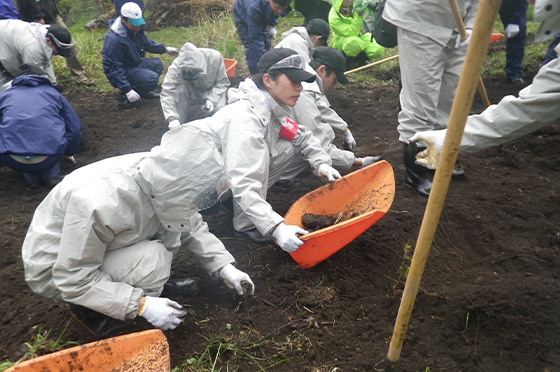 真っ白い作業服を着たクボタの研修生たちが、耕作放棄地にて土を掘り起こす作業に従事する