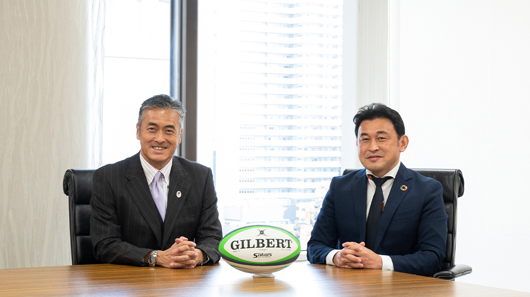 会議室で、ラグビーボールを前に笑顔で写真に収まる玉塚元一さん、石川充さん。