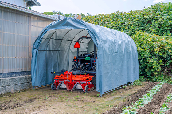 ほ場の隅に設置された簡易ガレージで保管されている、畝立て機が付いたクボタ製のトラクタ